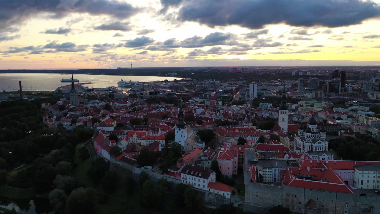 Filmato mozzafiato con drone del Centro Storico medievale di Tallinn al tramonto. L'inquadratura mostra la Collina di Toompea, la Cattedrale di Santa Maria e gli edifici dai tetti rossi sotto un cielo drammatico di nuvole rosa e arancioni.