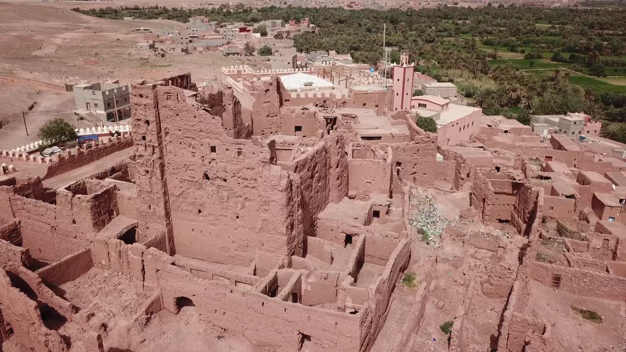 Aerial shot of a historic crumbling Kasbah palace in Ouarzazate. The red clay ruins contrast with the green oasis, showcasing Morocco's architectural heritage