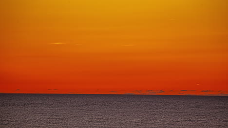 time lapse view of the sea disappearing into the horizon of the orange glow of the setting sun