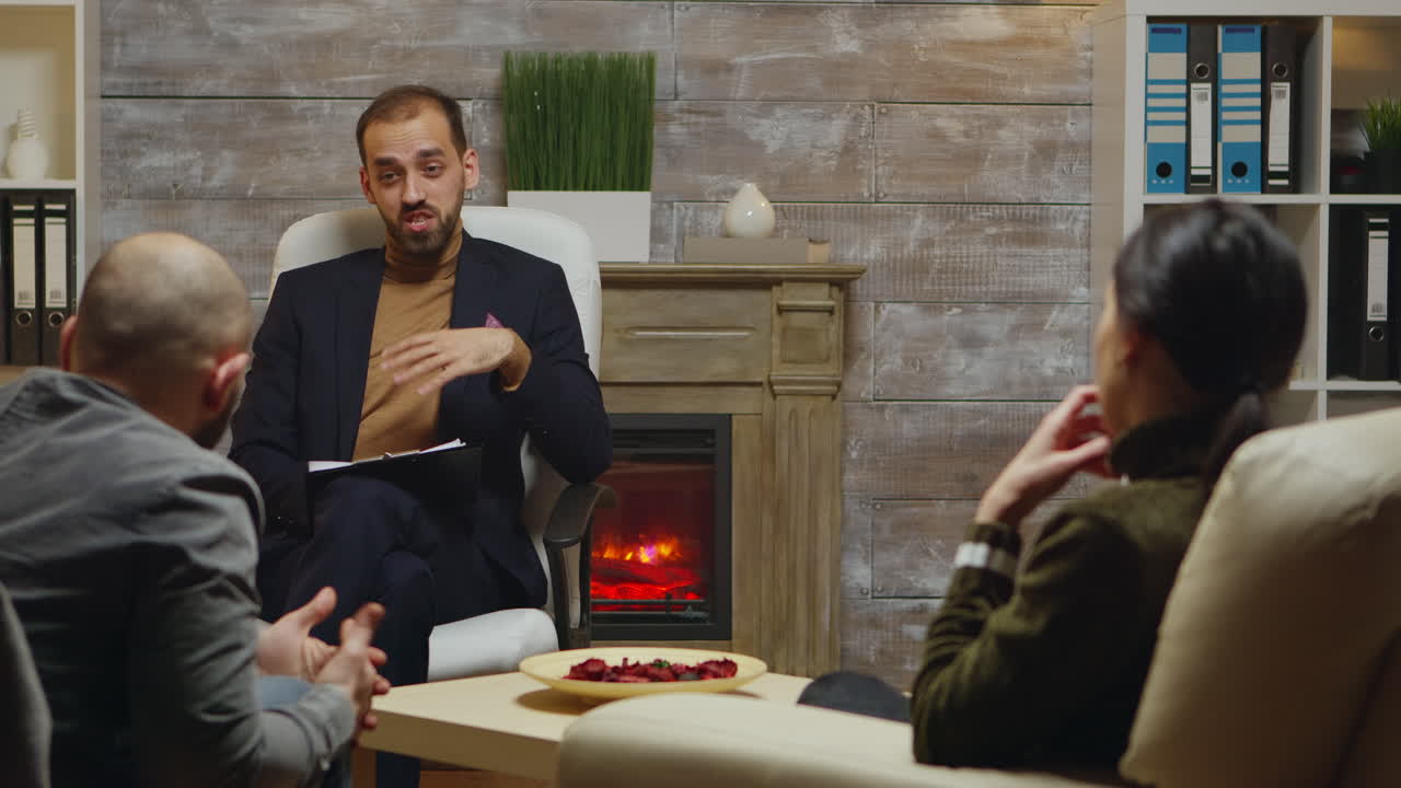 수염이 있는 심리 치료사가 젊은 부부를 돕고 있습니다.