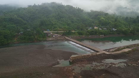 Dam-Spillway-Under-Road-Bridge-With-Foggy-Forest-Mountains-At-The-Background-In-Catanduanes,-Philippines