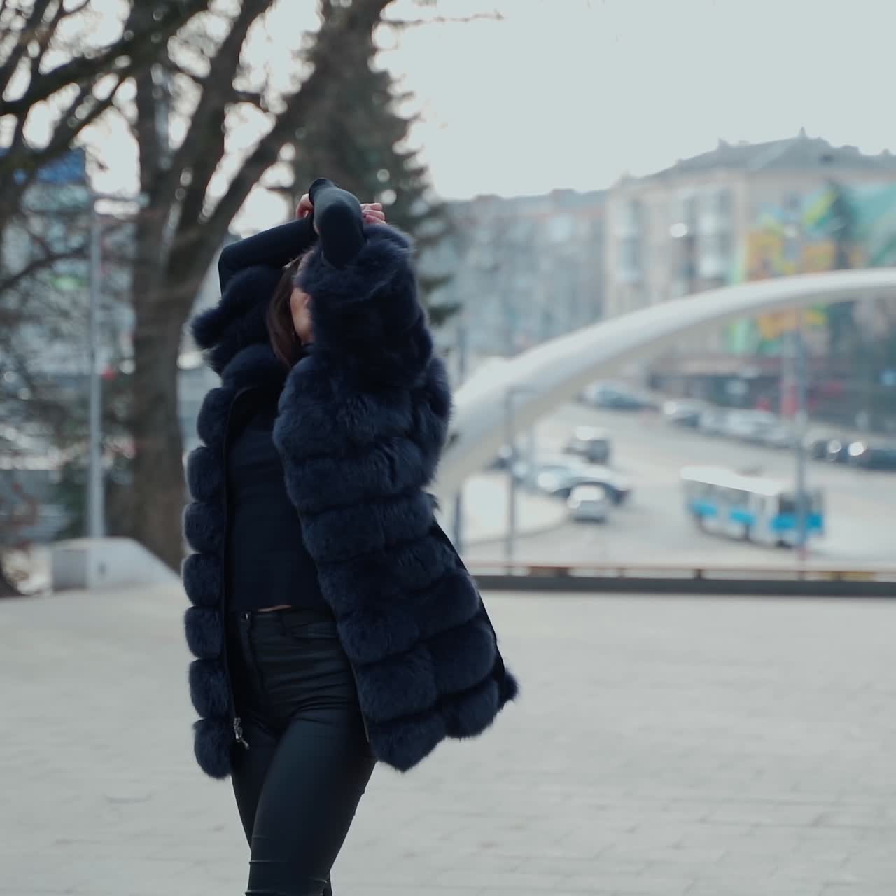 Attractive girl posing on camera in the city park. Beautiful model in black clothing walking outdoors. Lovely girl with opened fur coat. Slow motion.