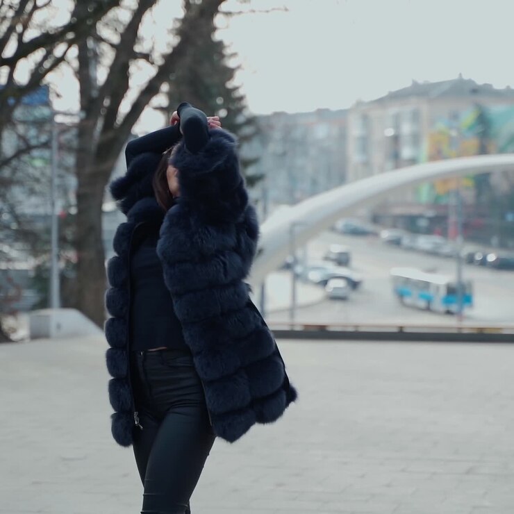 Attractive girl posing on camera in the city park. Beautiful model in black clothing walking outdoors. Lovely girl with opened fur coat. Slow motion.