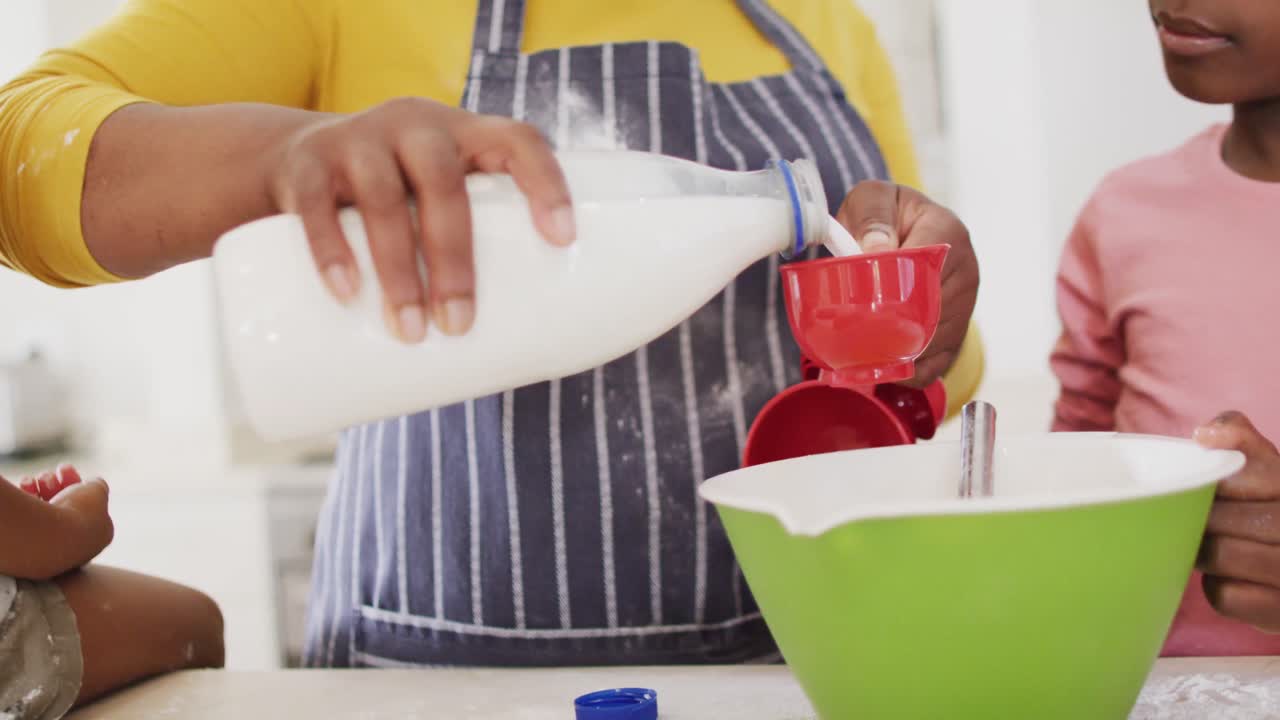 Midsection of african american grandmother baking with grandchildren in kitchen, slow motion