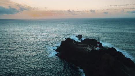 Dolly-Panorámico-Aéreo-Hacia-Atrás-Lejos-Del-Faro-Sobre-Rocas-En-Medio-Del-Océano-Azul