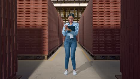 full body of asian female with her tablet with red brick packed in stacks are stored, typing on her tablet's keybaord with meditation