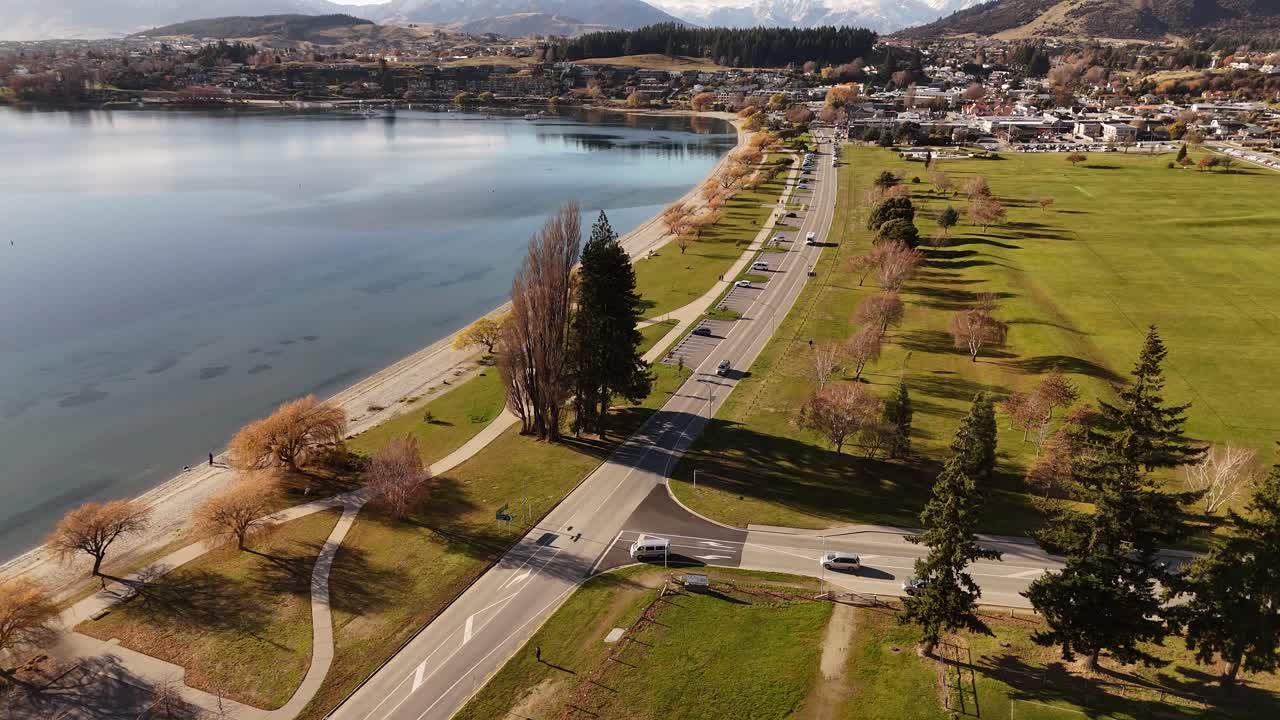 Auto che percorrono un incrocio su una strada costiera a Wanaka, Nuova Zelanda. Alba dorata in estate. Vista aerea dall'alto. Città e quartiere sullo sfondo