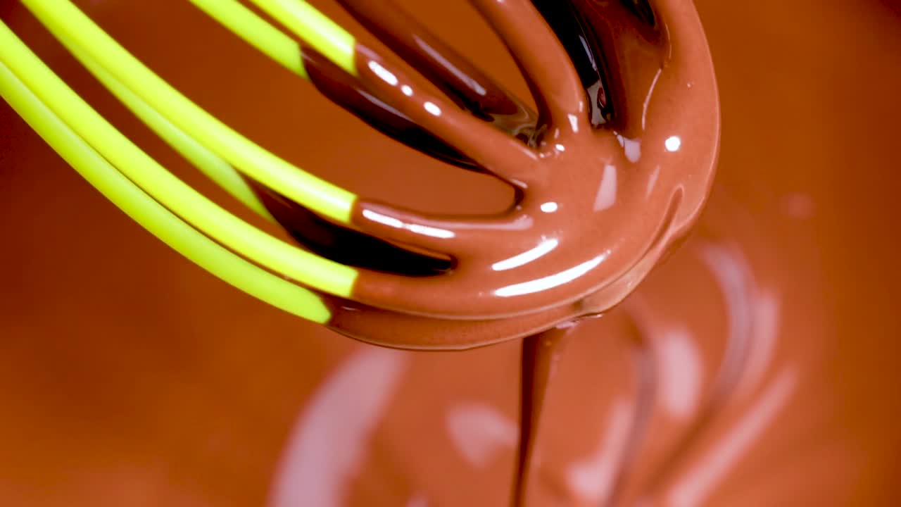 Vibrant green whisk blending rich, glossy chocolate in a smooth, swirling motion.