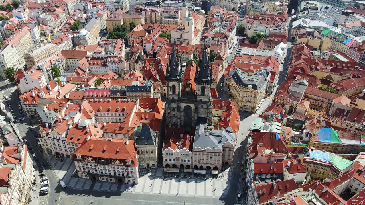 Historic Prague square, gothic cathedral tower over bright rooftops in summer sun