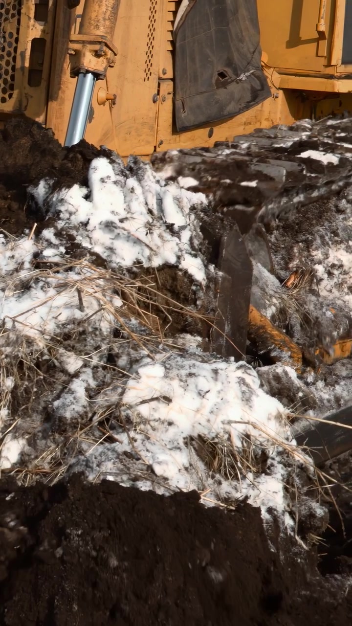 Neve e terra spinte da un bulldozer, primo piano di strati di terra congelata con fango bagnato e vegetazione strappata, giallo
