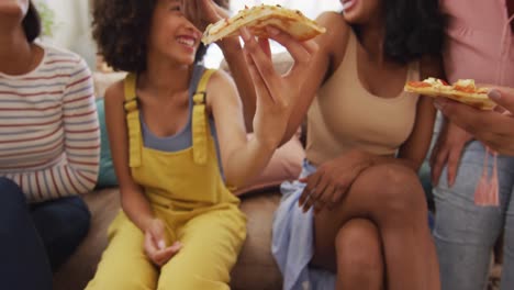 felices amigas diversas sentadas en el sofá en la sala de estar, comiendo pizza