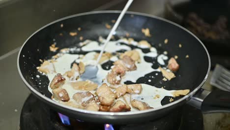 white cream sauce being poured over cut meat pieces in frying pan