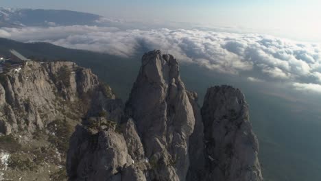 ai-petri rocky mountain above the clouds at sunny day. aerial view. drone is orbiting around. establishing shot.