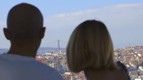 tourists admiring the view from la senora del monte in lisbon portugal, beautiful rooftops and the vasco da gama bridge in the distance