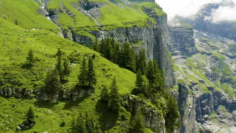 flying over beautiful, green mountains in switzerland with a small house located on slope