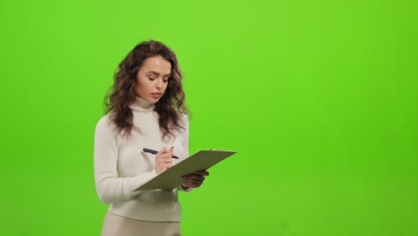 a woman is making notes in the document. she's focused. she is raising her head and looking at the camera. she is standing on a green background. green screen. 4k.