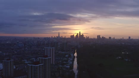 telephoto dolly back aerial drone shot of london canal towards city skyline at sunset