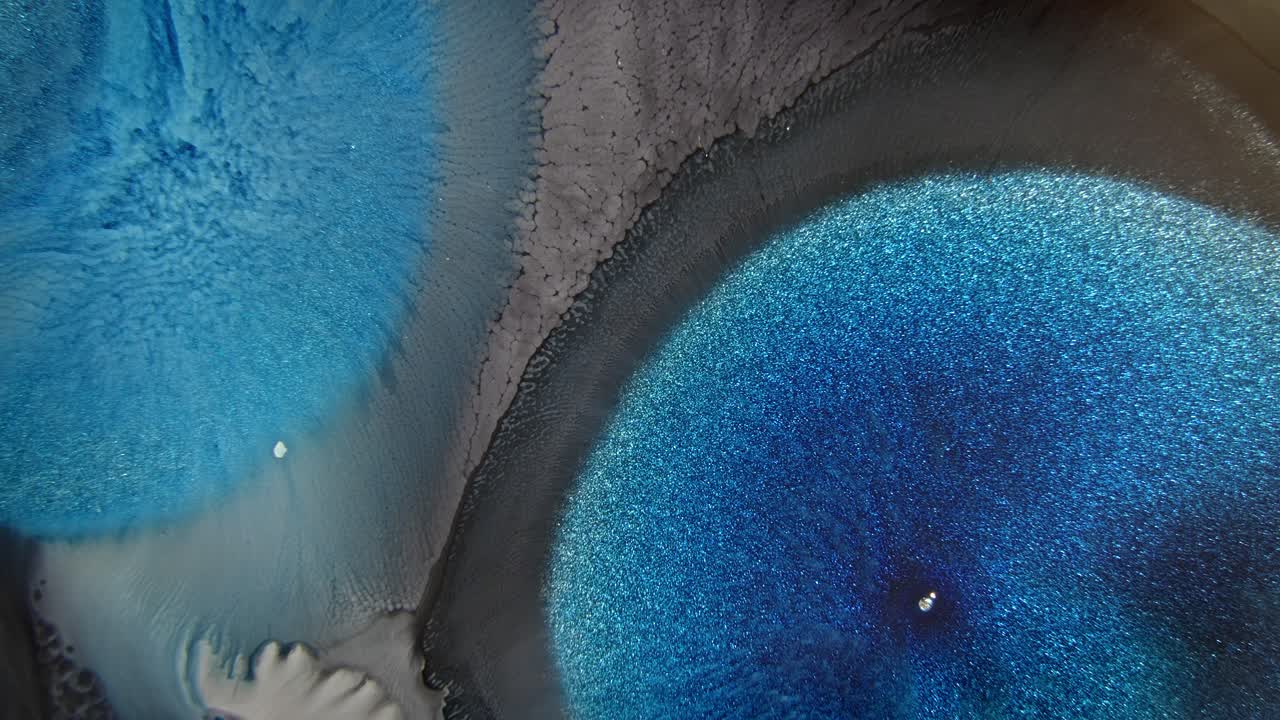 tinta azul en agua con partículas brillantes creando un efecto de doble textura, que recuerda a un fenómeno cósmico
