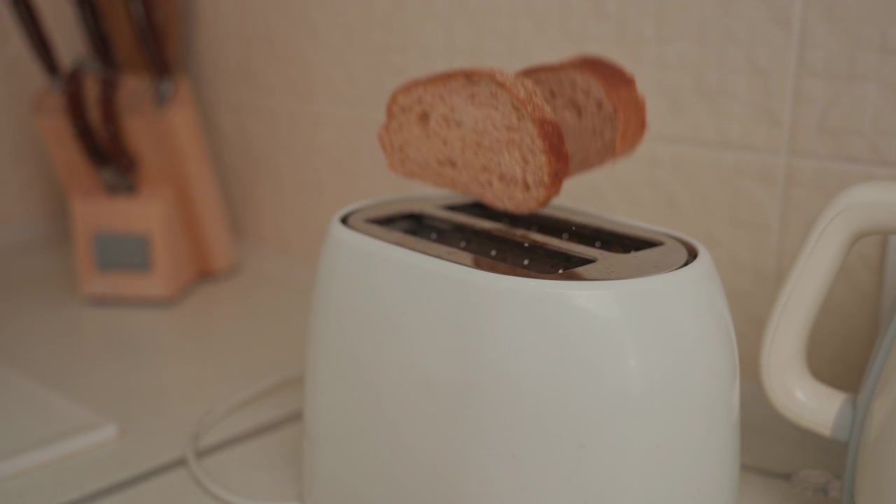 Toaster on counter ejects bread, ambient soundtrack for music lover, white toaster and kettle, knife block background, slow pop motion, warm light, crumb detail, cozy domestic scene