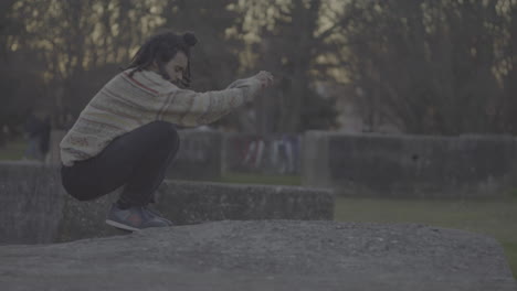 man jumping and squatting in a park at sunset