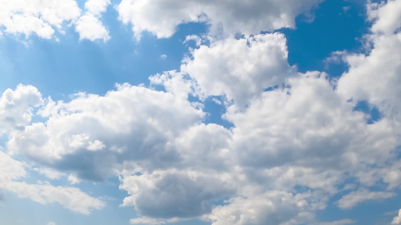 Cumulus white clouds moving by the sky. Soft fluffy cloudscape in the rays of bright summer sun. Low angle view. Timelapse.