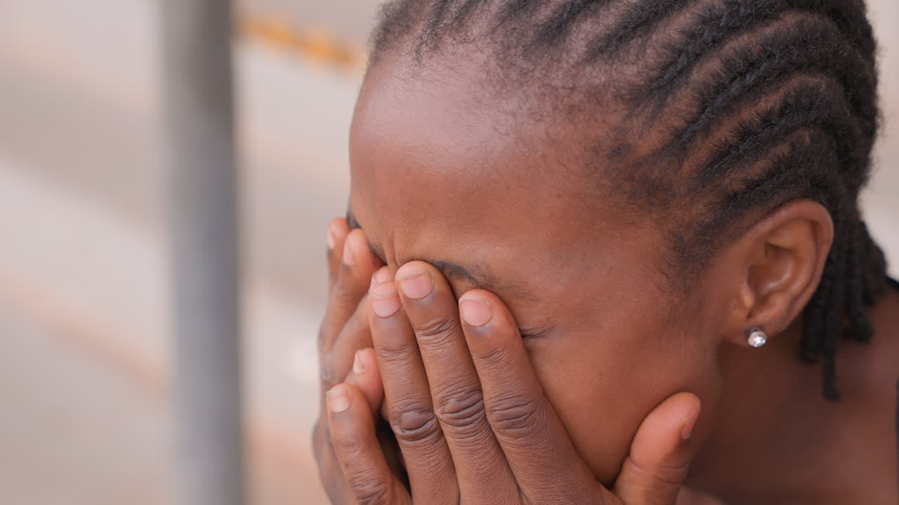 closeup distressed young woman covering face and rubbing eyes, braided hair, tense shoulders and tearful expression urban stairwell, candid close sequence of raw emotion showing anxiety, coping