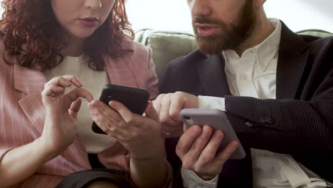 close up of woman and man in formal wear using mobile phone and talking together while sitting on sofa