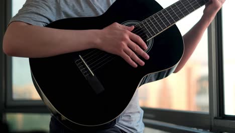 man playing a black acoustic guitar by a window