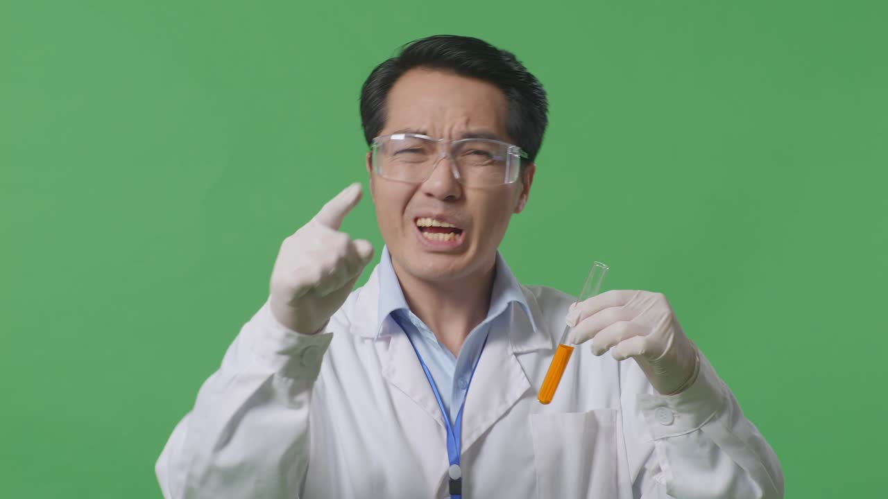 Close Up Of Angry Asian Man Scientist Looking At The Orange Liquid In The Test Tube And Shouting To Camera While Standing On The Green Screen Background In The Laboratory