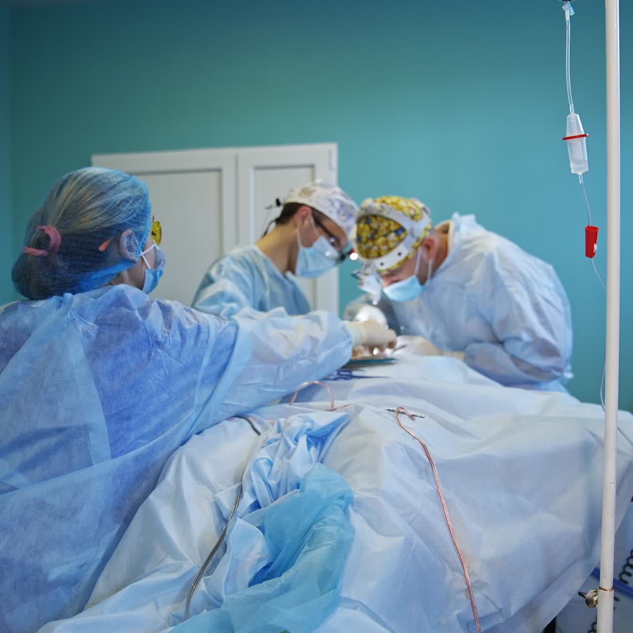 Team di chirurghi composto da due medici che operano il paziente in una sala operatoria normale. Un'infermiera posiziona gli strumenti sul paziente più vicino ai medici.