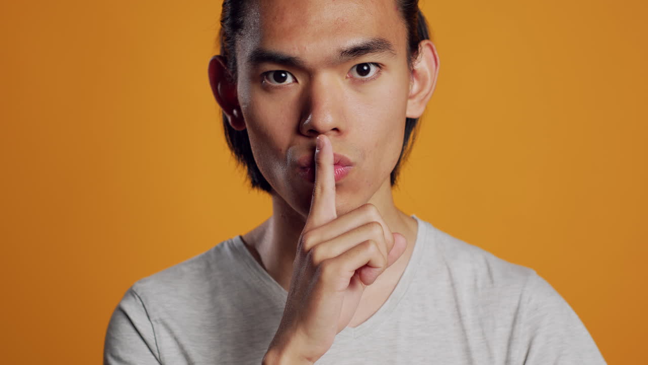 Private asian guy doing hush silent sign on camera