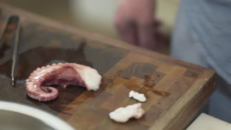 primer plano de las manos del chef cortando el pulpo en una bandeja de madera