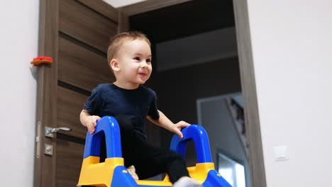 baby boy raising by the stairs of the plastic slide. happy toddler slides down cheerfully.