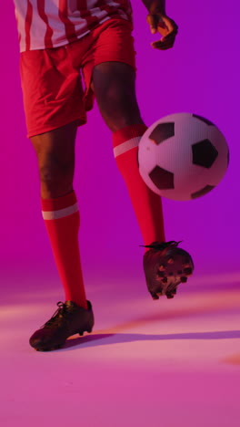 video vertical de un jugador de fútbol masculino afroamericano con fútbol sobre iluminación rosada
