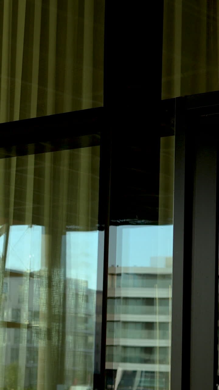 Uno scatto verticale che mostra i riflessi architettonici di moderni edifici cittadini in una grande finestra di vetro con cornici scure. Ideale per lo sviluppo urbano e il marketing immobiliare