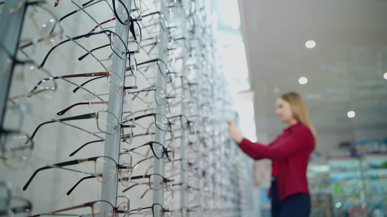 Fashionable eyeglasses in the optical store. Stand with new eyeglasses and a young woman choosing glasses. Vision concept.