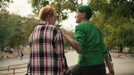 Rear-view-of-a-girl-with-short-green-hair-in-a-green-shirt-straightens-the-hair-of-her-girlfriend-with-yellow-hair-in-a-plaid-shirt.-Lesbian-couple-on-a-date-at-the-skate-park