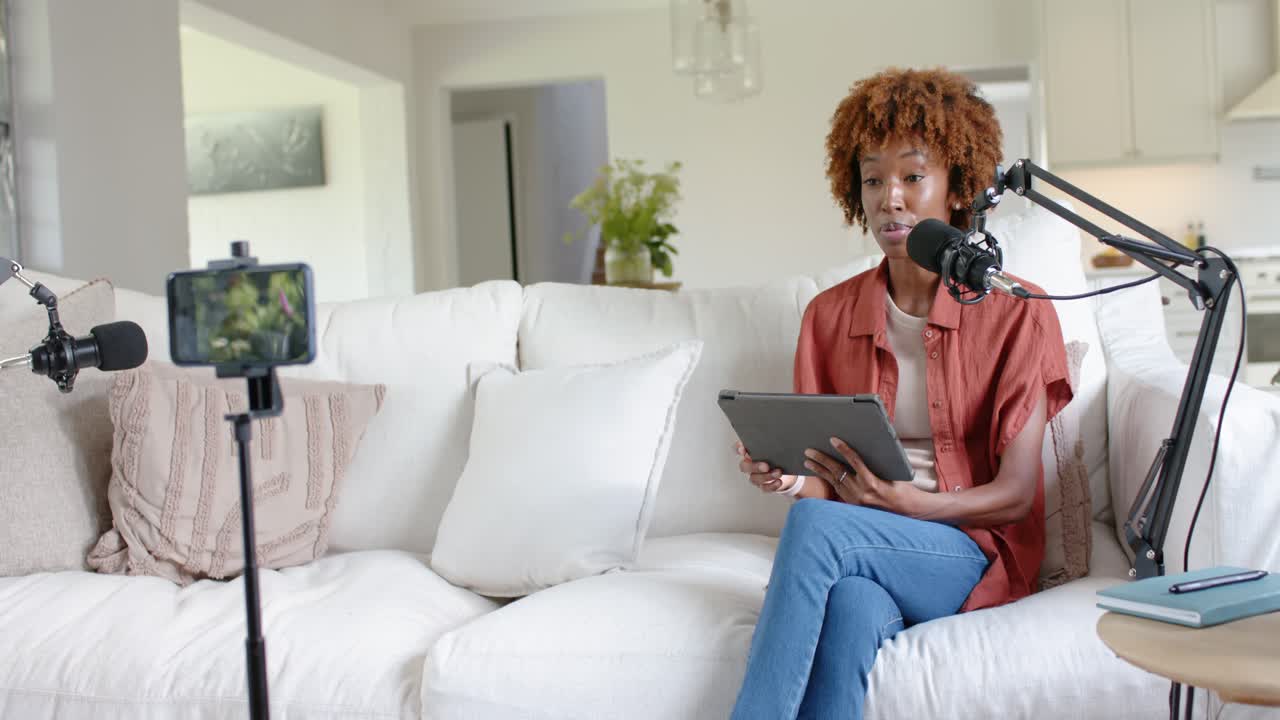 Donna afroamericana adulta che registra a casa, legge un tablet, parla al microfono del telefono, con spazio per il testo