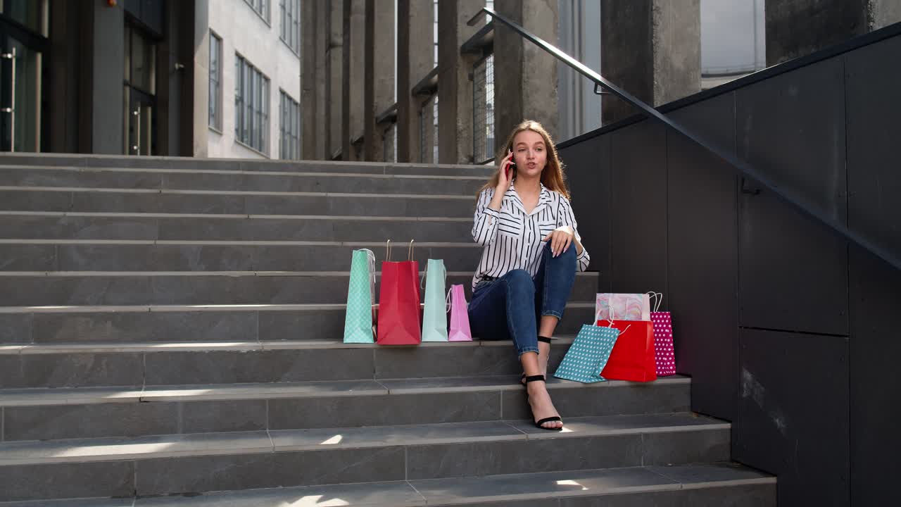 chica sentada en las escaleras con bolsas hablando en el teléfono móvil sobre la venta en el centro comercial en black friday