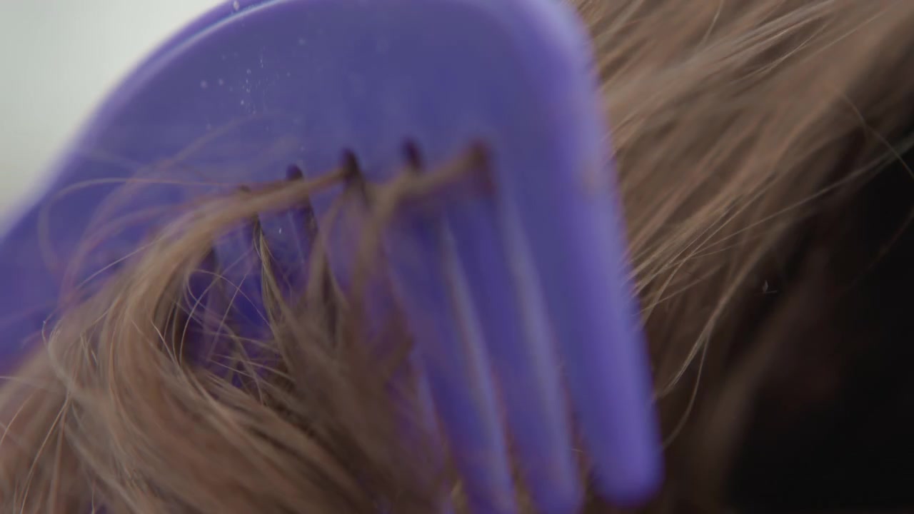 Close view shows comb moving through long brown hair, creating visible separation, soft sheen, gentle flowing movement, and fine flyaways under neutral light with clean grooming texture