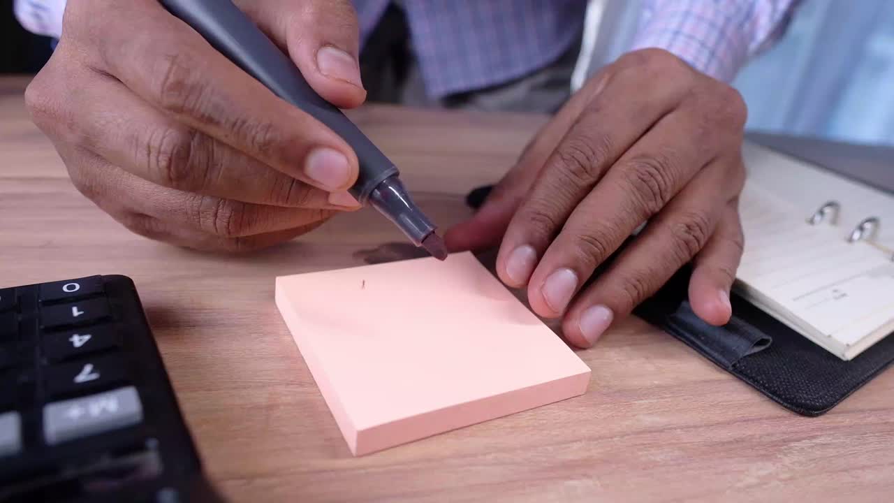 Person Writing on a Sticky Note at a Desk