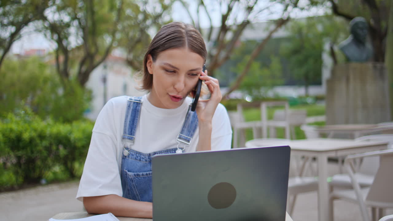 Girl startuper talking smartphone looking laptop screen at outdoors cafe closeup