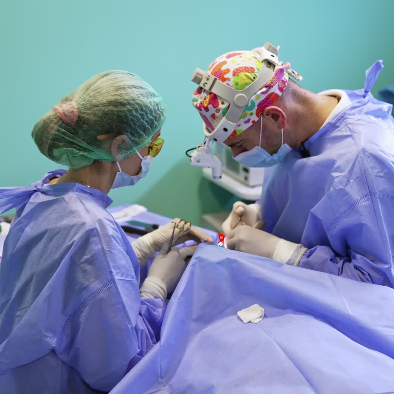 Male surgeon makes stitches with thread and forceps. Final stage of procedure. Female medic assisting