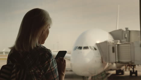 woman traveler uses a smartphone in the airport terminal on the background of a large airliner outsi