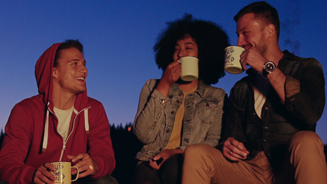 친구 들 이 캠프 불 에서 음료 를 즐기고 있다