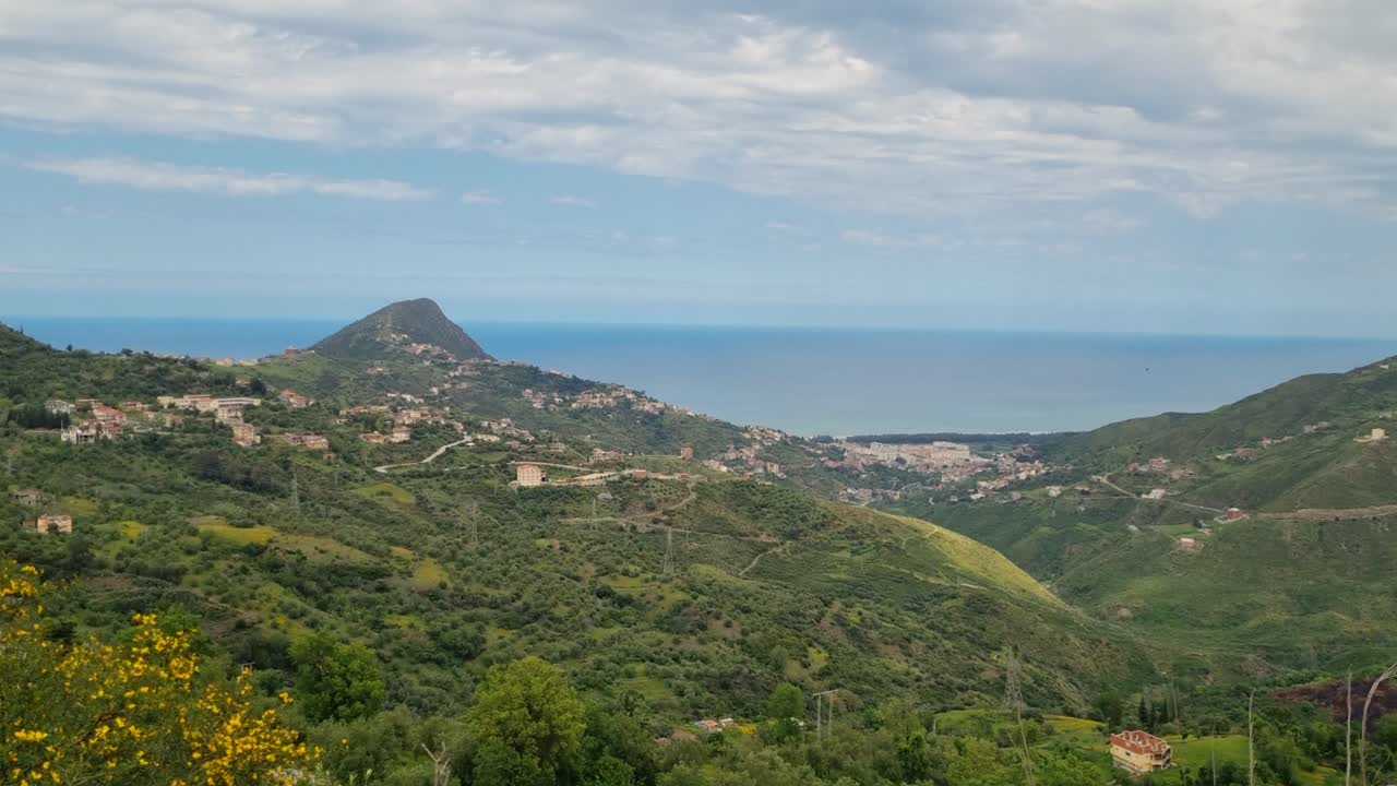 Vista panoramica della Cabilia, Algeria, con dolci colline verdi e villaggi in cima alle colline che si estendono fino al Mar Mediterraneo, mostrando un vasto paesaggio scenografico in una giornata di sole.