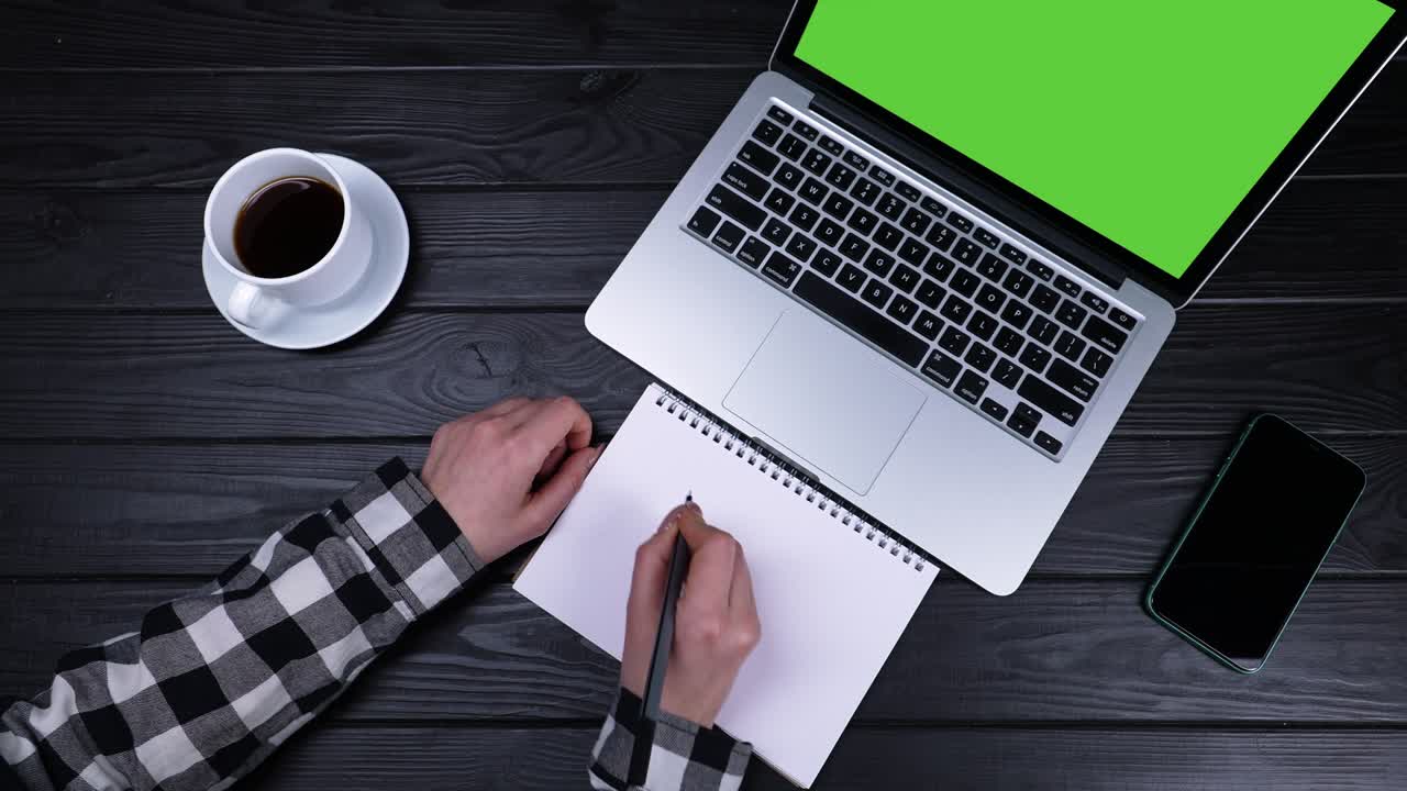 Sale 50 percent, girl writes a note with a pen in a spiral notebook from a laptop with a green screen. Top view of the hands of a girl who sits at a desk a laptop and a phone. Slow motion. Close up