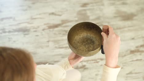 woman playing bowl gong with mallet against fireplace