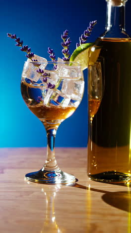 a refreshing cocktail with ice, lime, and lavender next to a bottle against a blue background