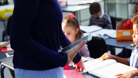 Teacher-using-digital-tablet-while-teaching-in-classroom